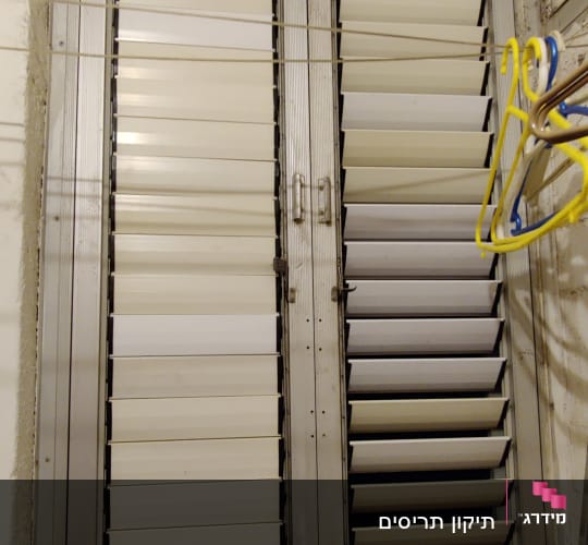 תריסים לבנים עם מסגרת מתכת בחלון